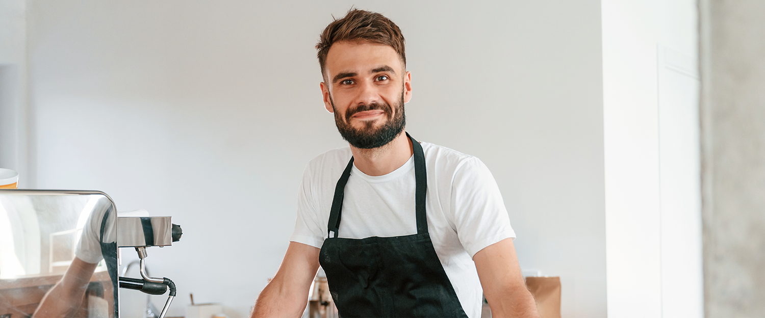 A portrait of a barista standing next to their coffee machine in a cafe